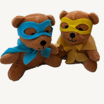 Two brown plush superhero teddies, one blue and one yellow, seated together on a light background