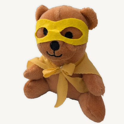 Brown plush teddy wearing a yellow superhero mask and cape, shown seated against a light background